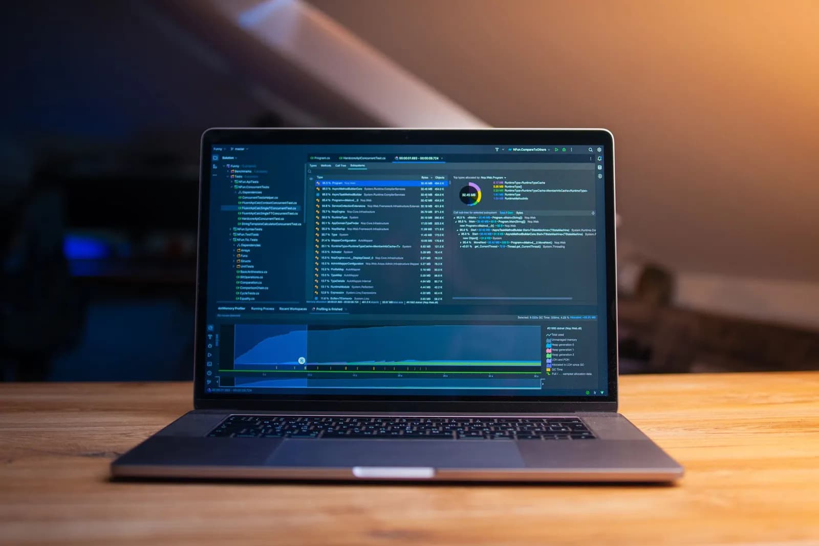 A laptop displaying code on a wooden desk, in a dimly lit workspace.