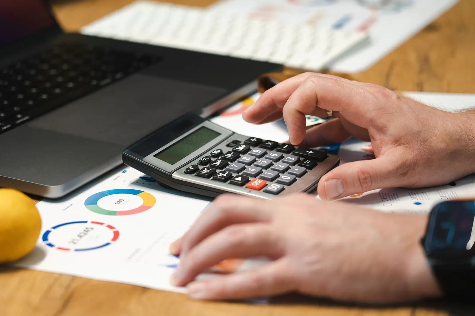 Close-up of hands calculating financial data with reports, smartphone, and cash on table.