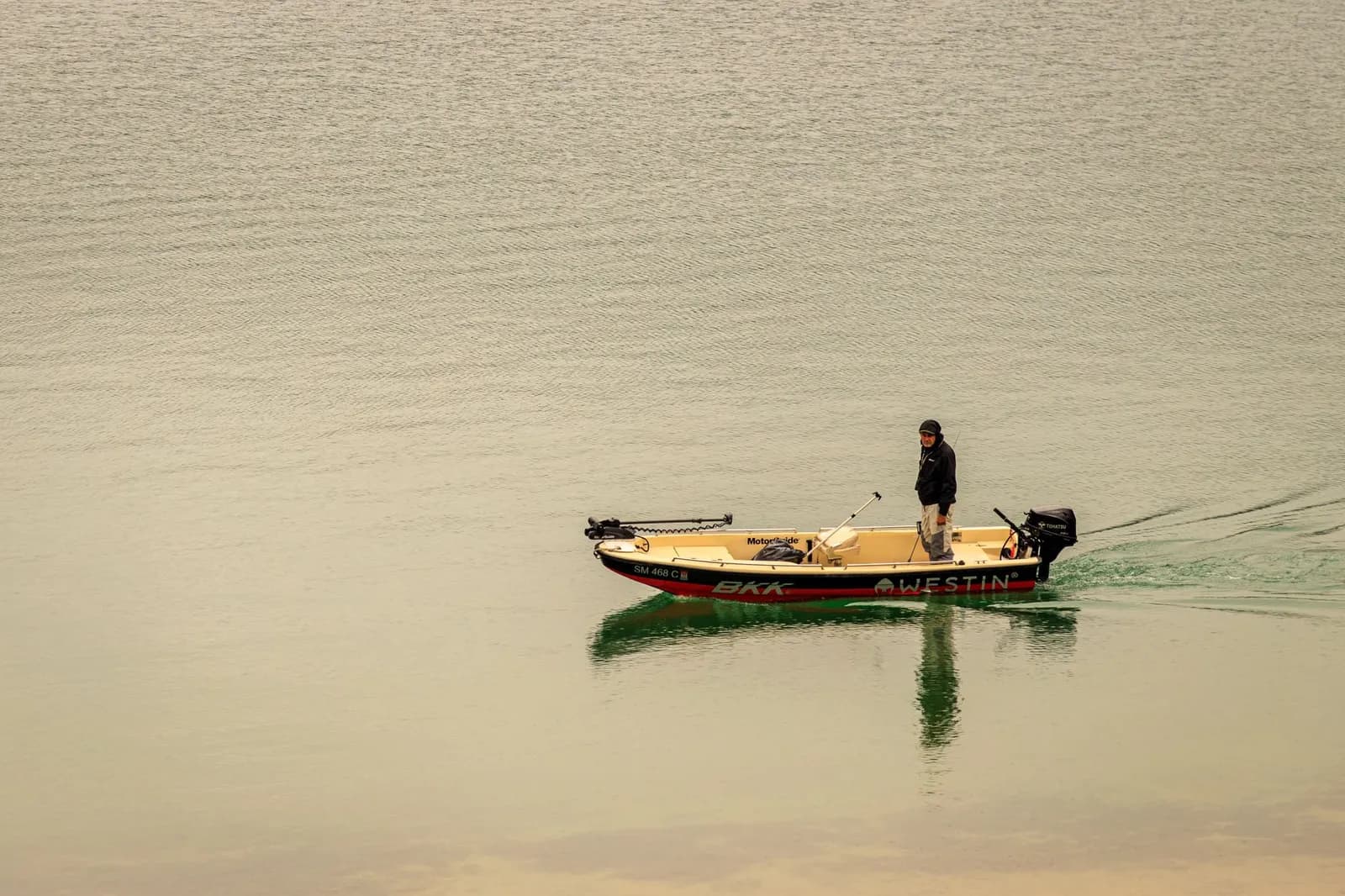 A lone man fishing on a calm lake in Serbia from a motorboat during the day.
