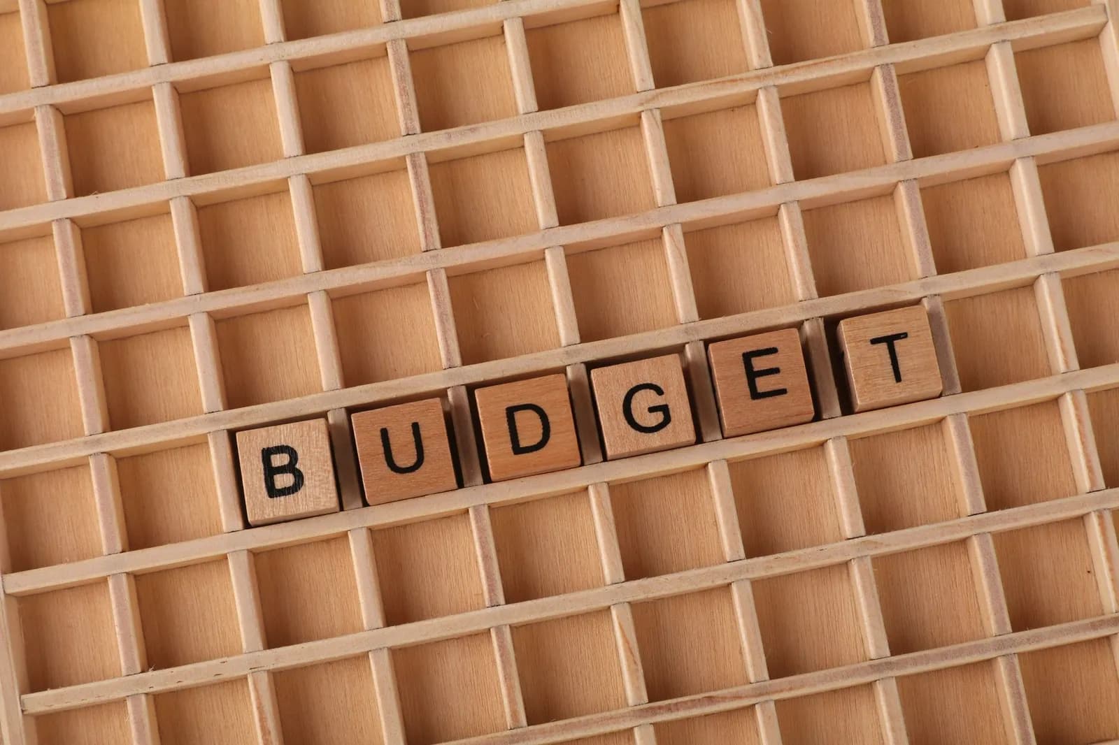 Wooden letter tiles spelling 'budget' on a wooden grid background, symbolizing finance and planning.