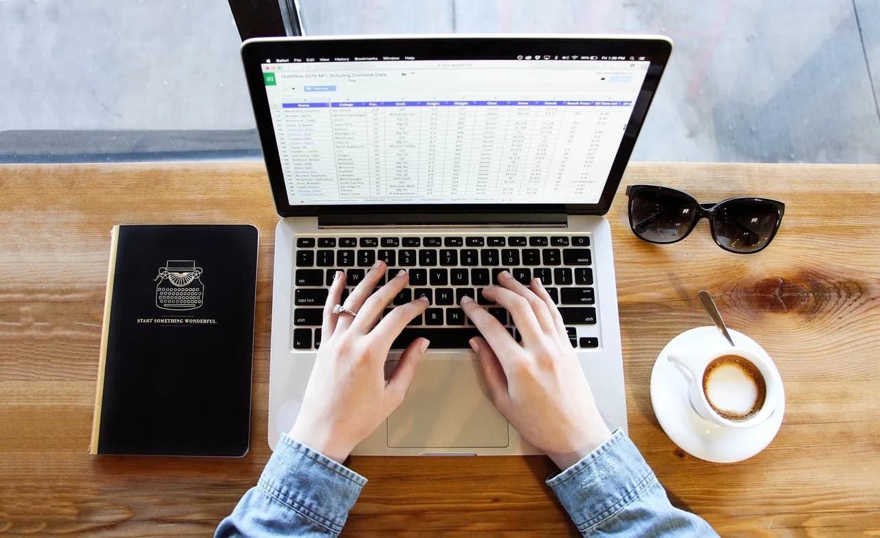 Hands typing on MacBook Air with Google search open, coffee nearby.