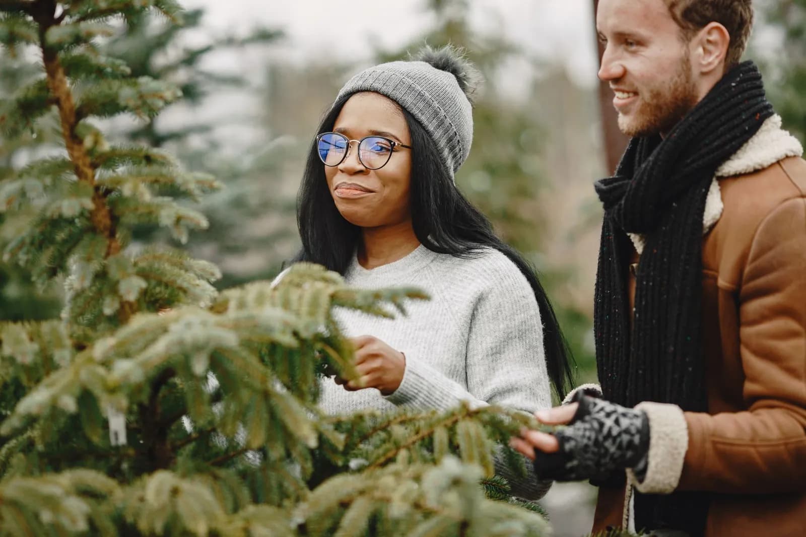 Smiling couple in winter clothing selecting a Christmas tree outdoors. Perfect for holiday-themed content.