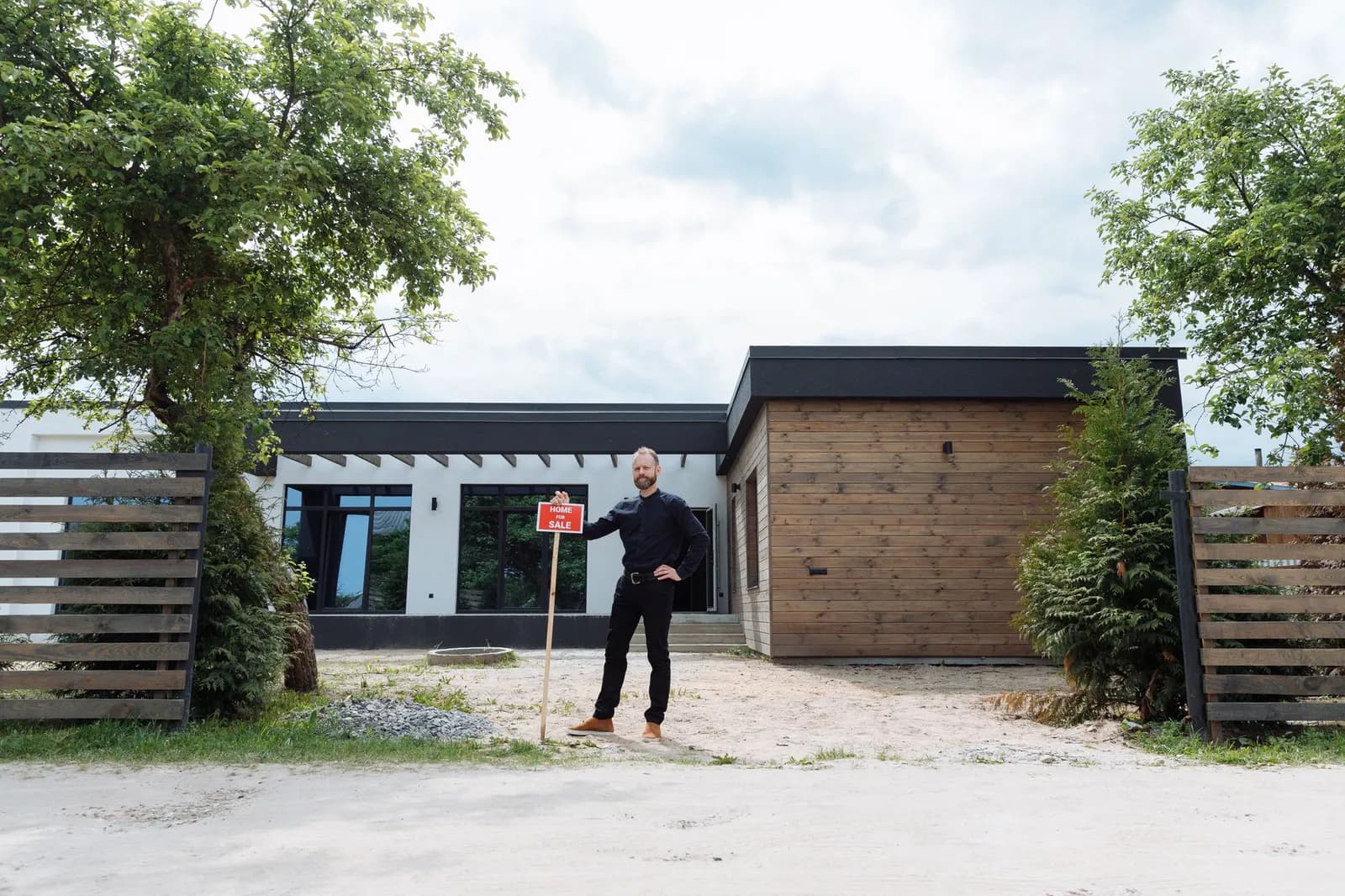 Real estate agent standing outside modern house with for sale sign, featuring contemporary design.