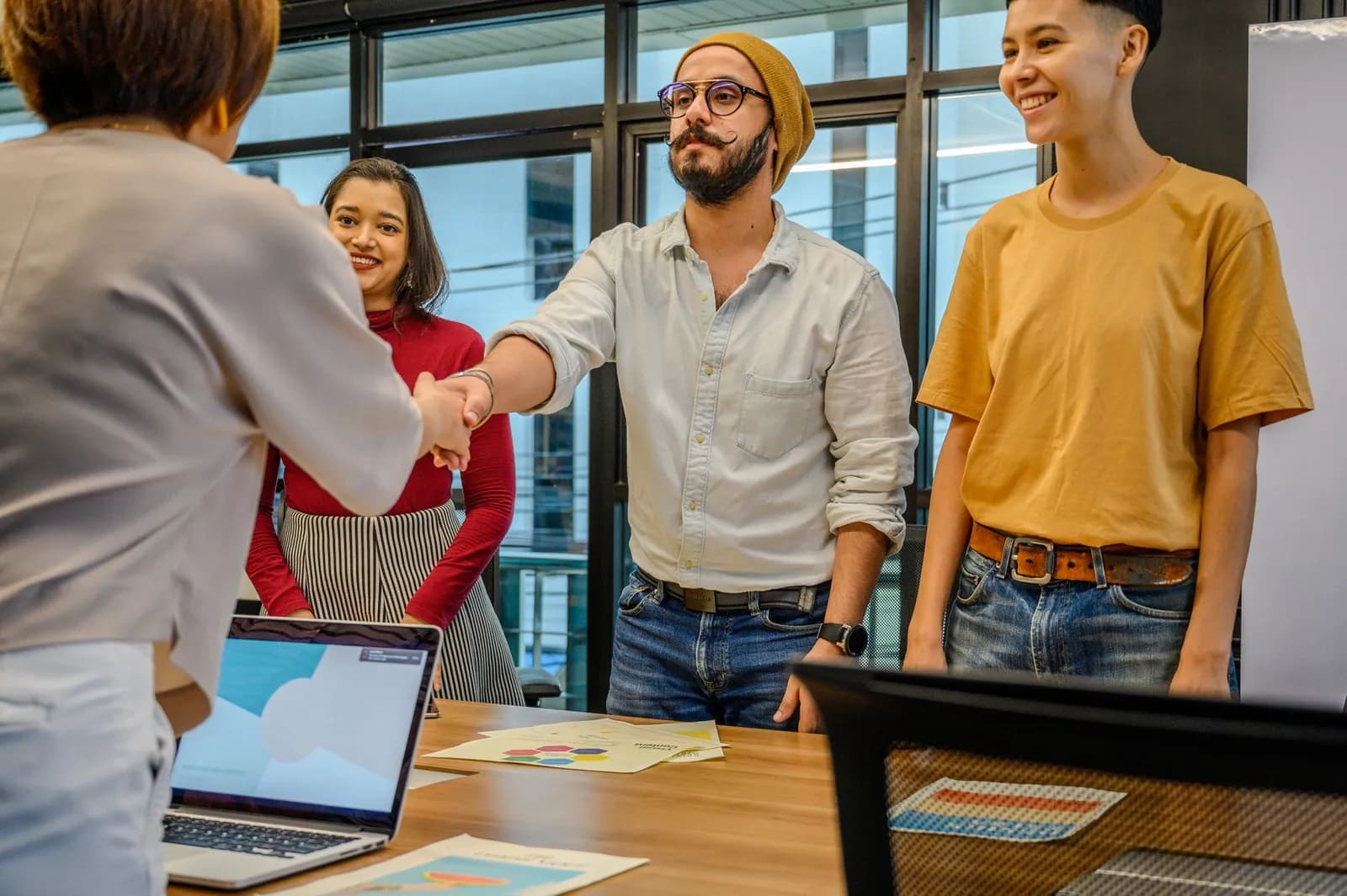 Multiracial coworkers in formal outfit shaking hands near table with scales of justice