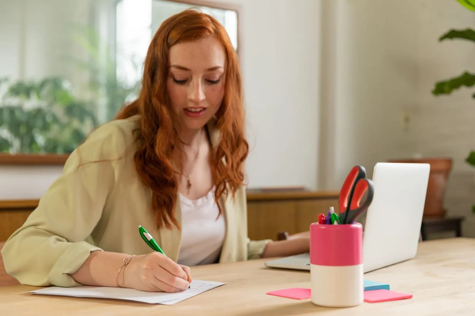Focused woman writing at desk with Lady Justice figurine and certificate in office.