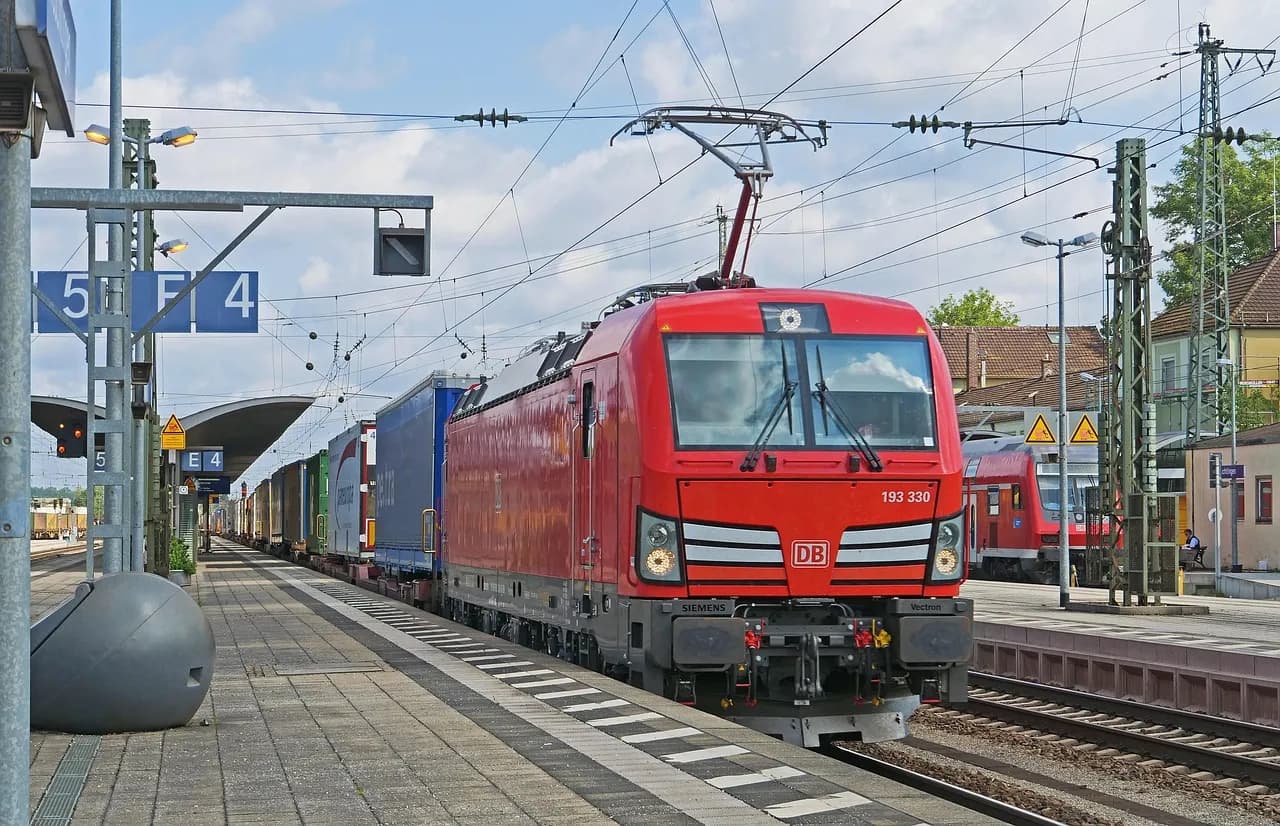 Cargo train parked at a modern urban railway station on a cloudy day.