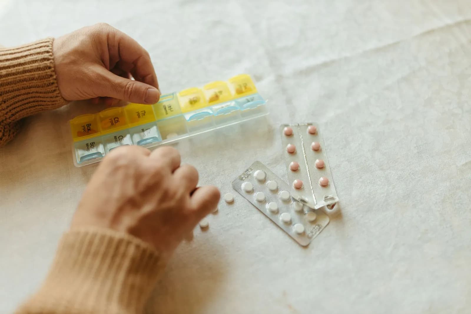 Close-up of hands organizing tablets into a weekly pillbox for daily medication management.