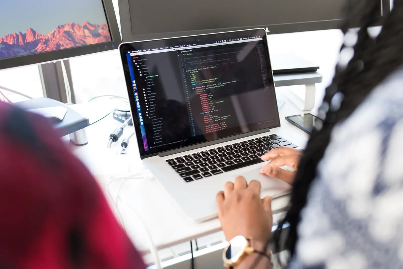 Coding setup with laptop displaying code and smartphone on a wooden table, ideal for tech themes.