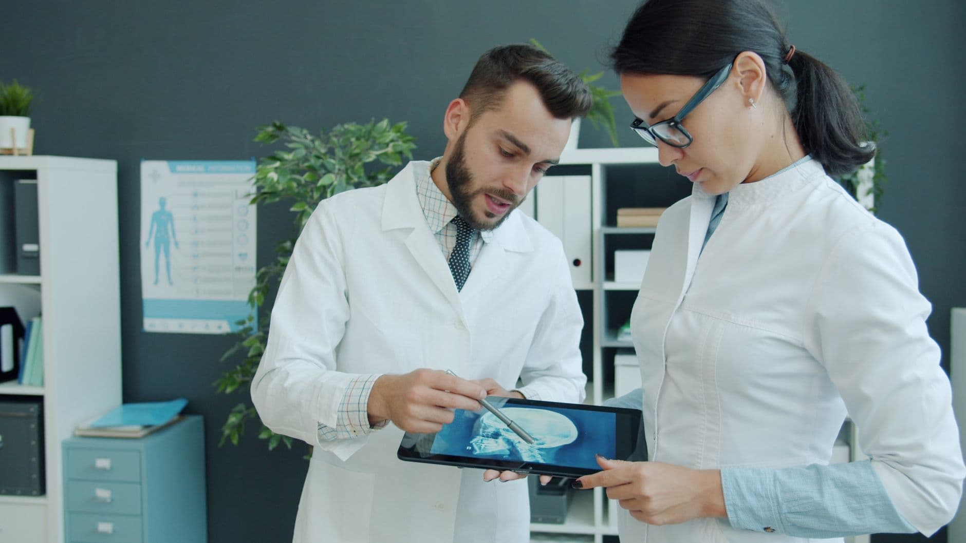 Doctors examining a patient's X-ray on a tablet in a medical office.