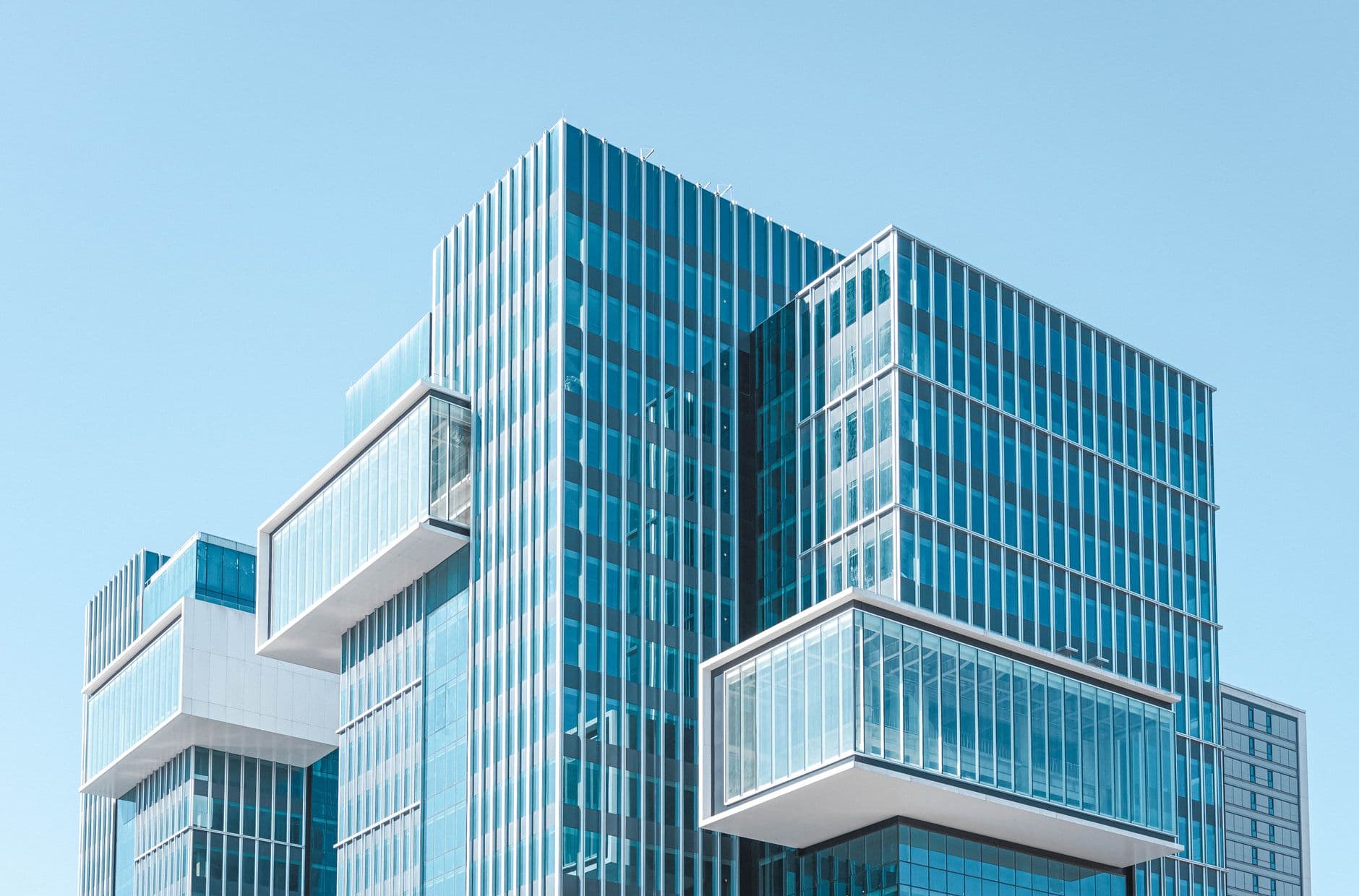 Striking contemporary glass building with unique geometric extensions under clear blue sky.