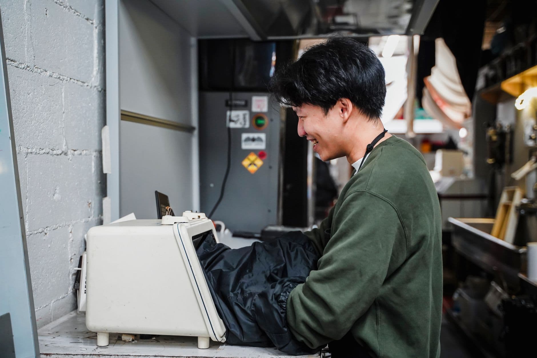 Young man smiling while operating industrial machinery in a factory setting.