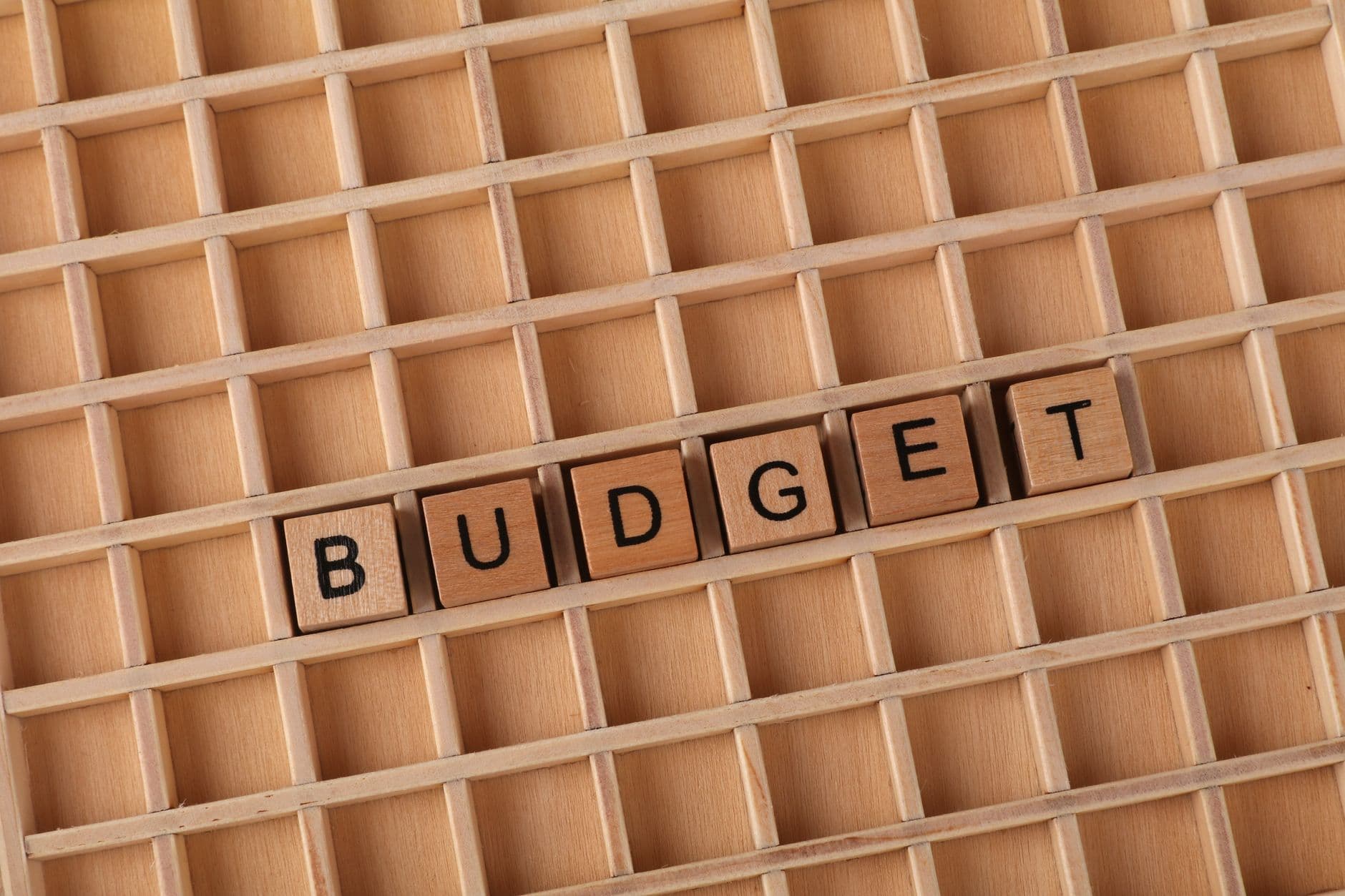 Wooden letter tiles spelling 'budget' on a wooden grid background, symbolizing finance and planning.