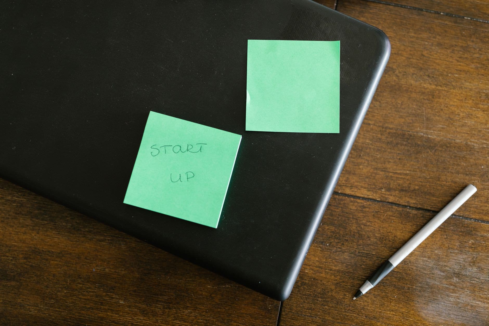 A laptop with green sticky notes and a pen on a wooden desk, symbolizing startup planning.