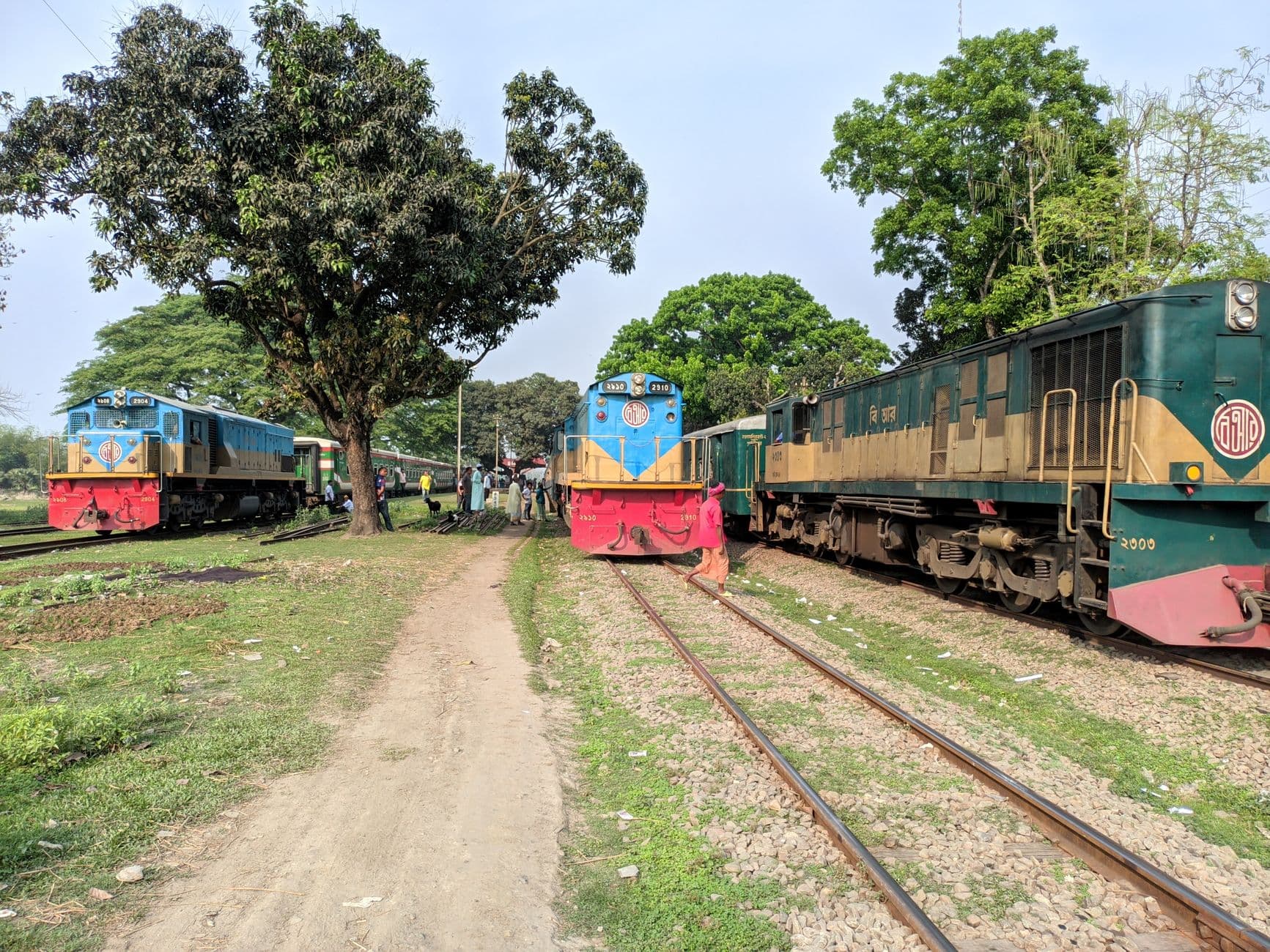 A lively railway scene in Bangladesh with trains, people, and lush greenery.