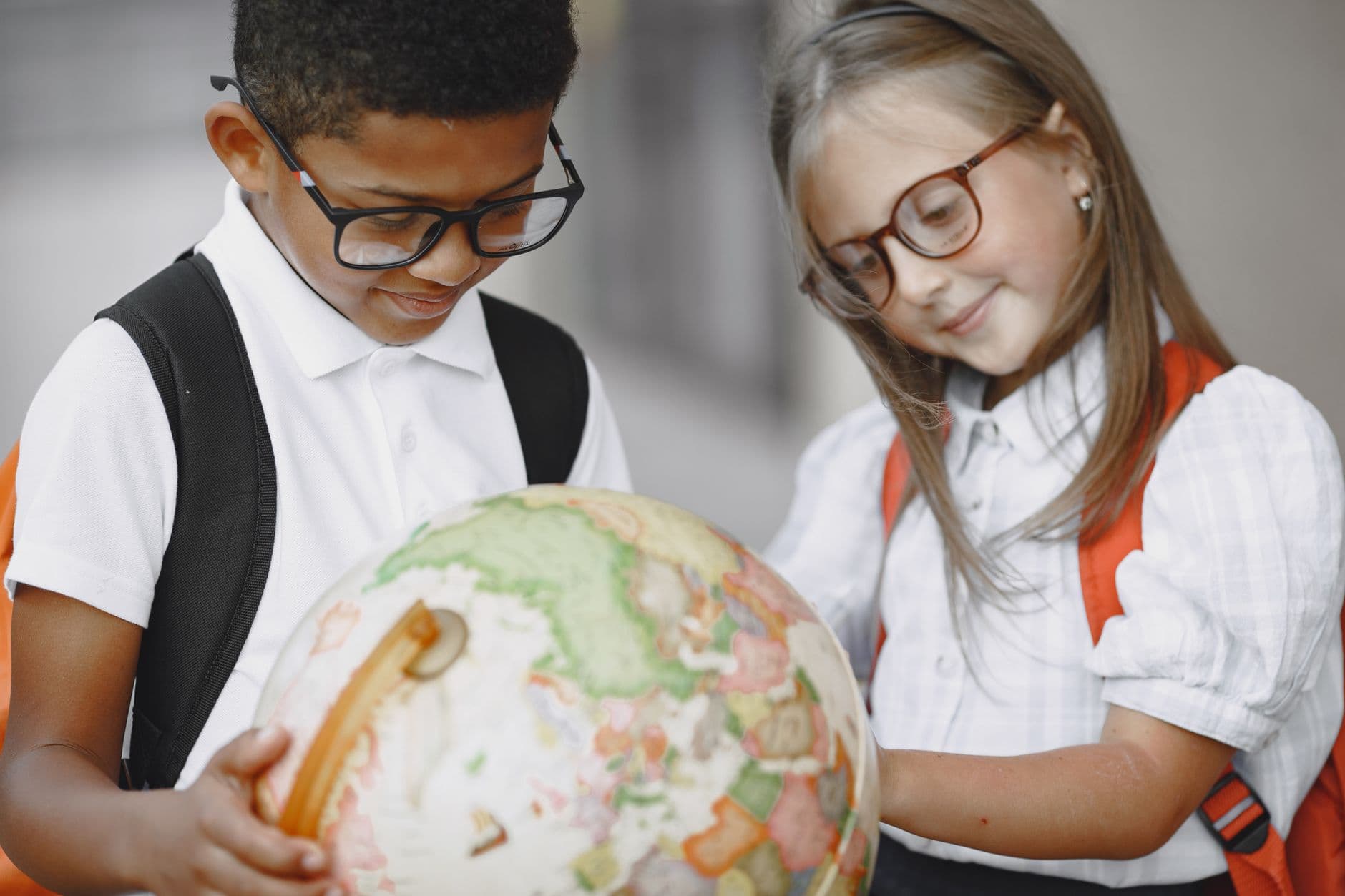 A girl and boy exploring a globe, learning geography together.