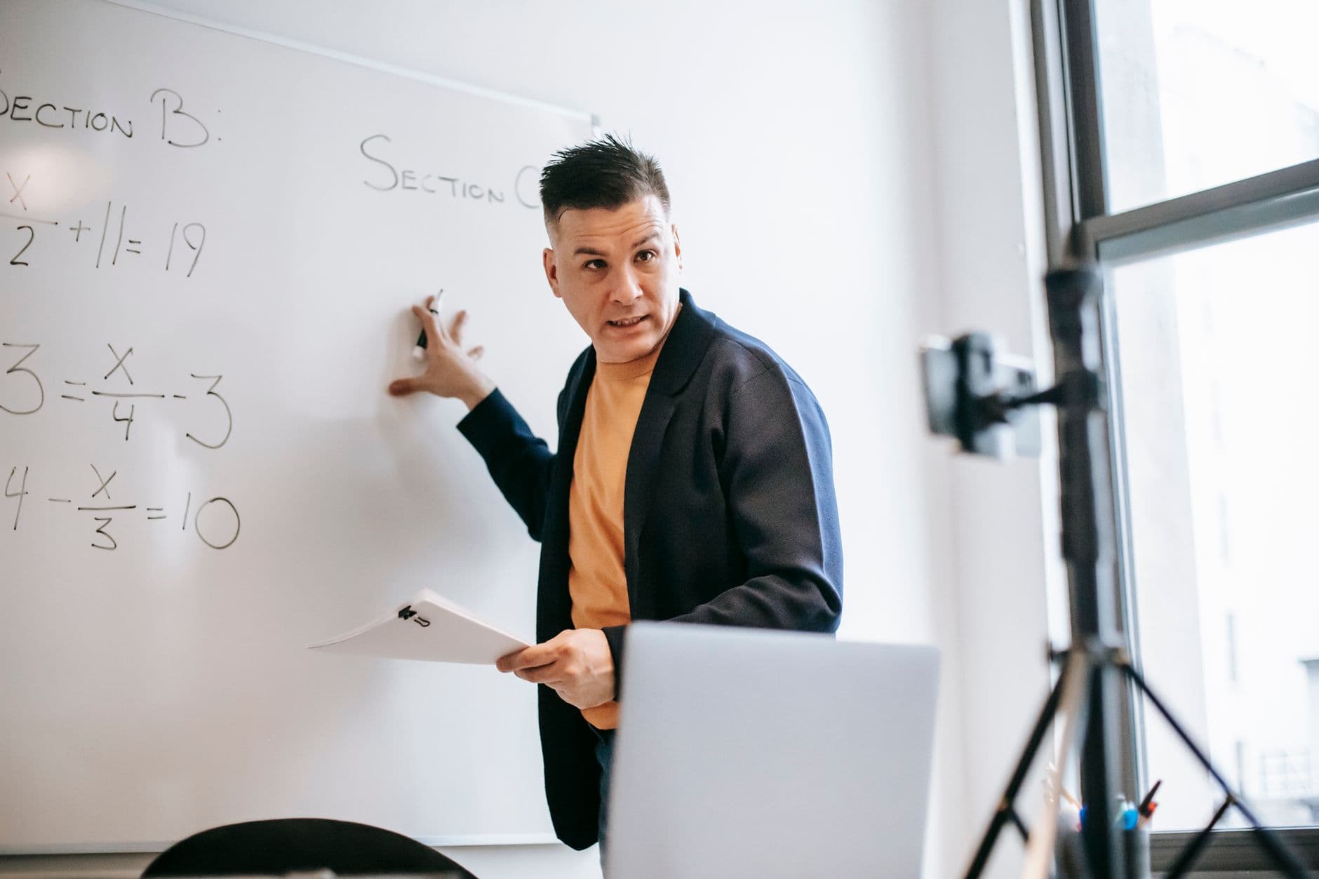 A male teacher explains math equations on a whiteboard during an online class.