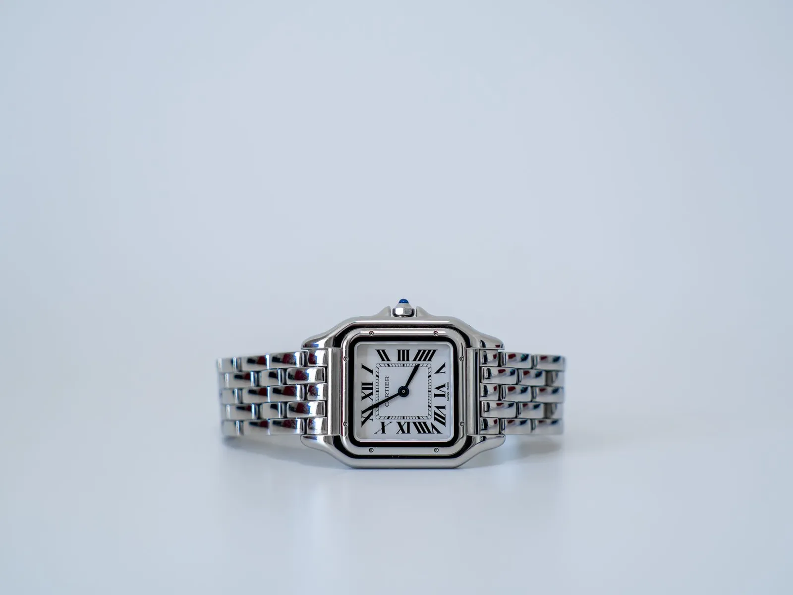 Close-up of a stylish silver watch featuring Roman numerals on a minimalist background.