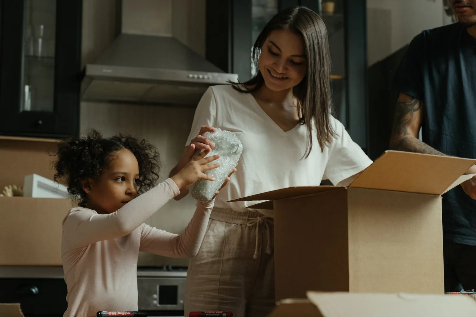 A young woman unpacks online shopping orders in a stylish modern kitchen, using her laptop for work.