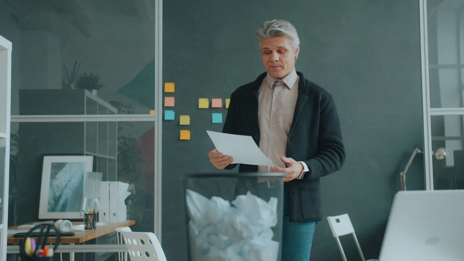 Mature man reviewing documents in a contemporary office setting with note wall in the background.