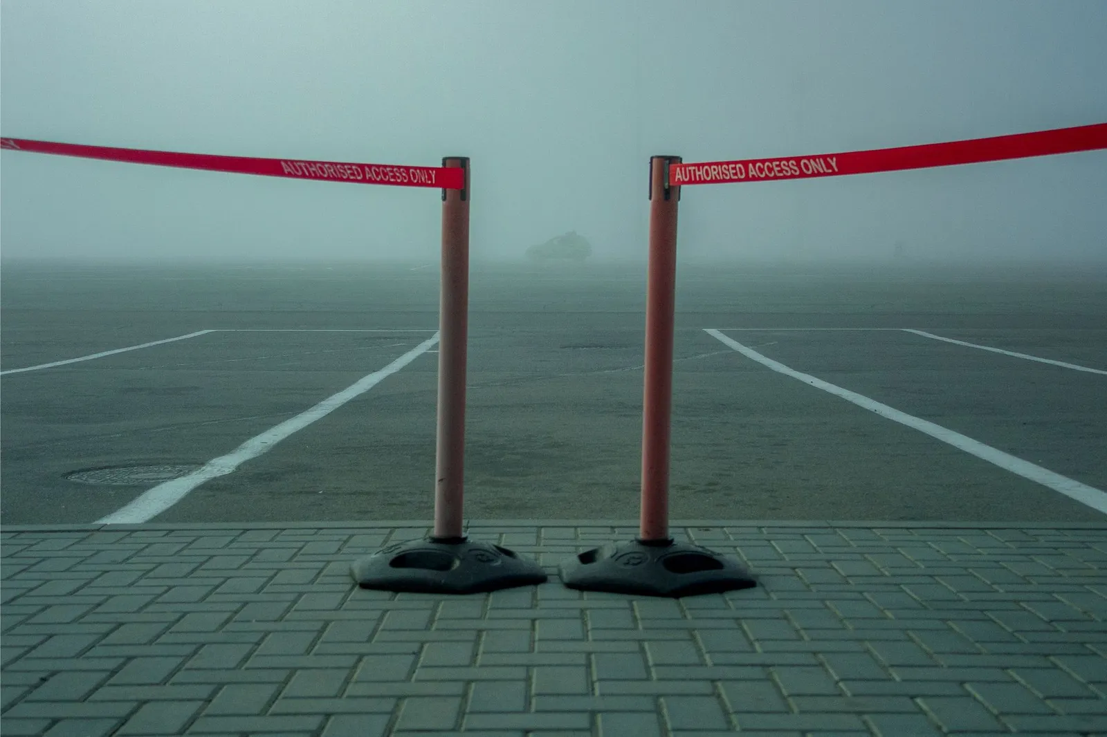 A foggy parking lot featuring a retractable barrier tape labeled 'AUTHORIZED ACCESS ONLY.'