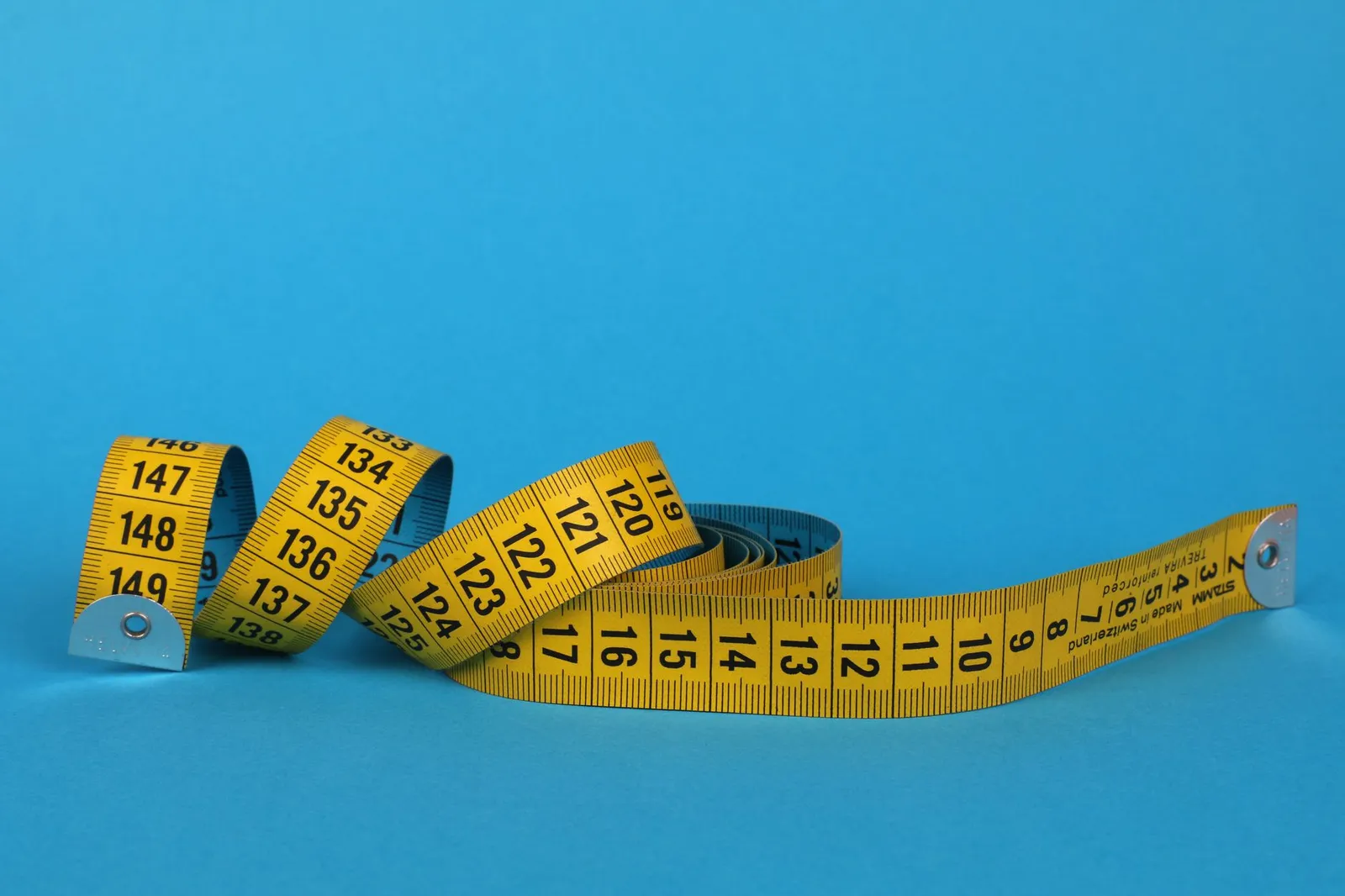 Coiled yellow measuring tape against a vibrant blue background, offering ample copy space.