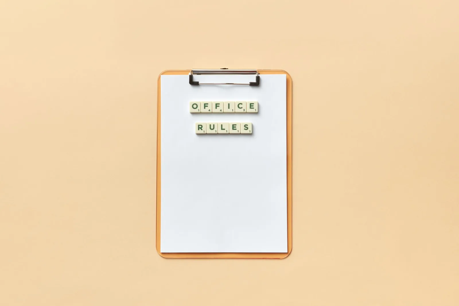 A clipboard with the phrase 'Office Rules' spelled out using Scrabble tiles on a beige background.