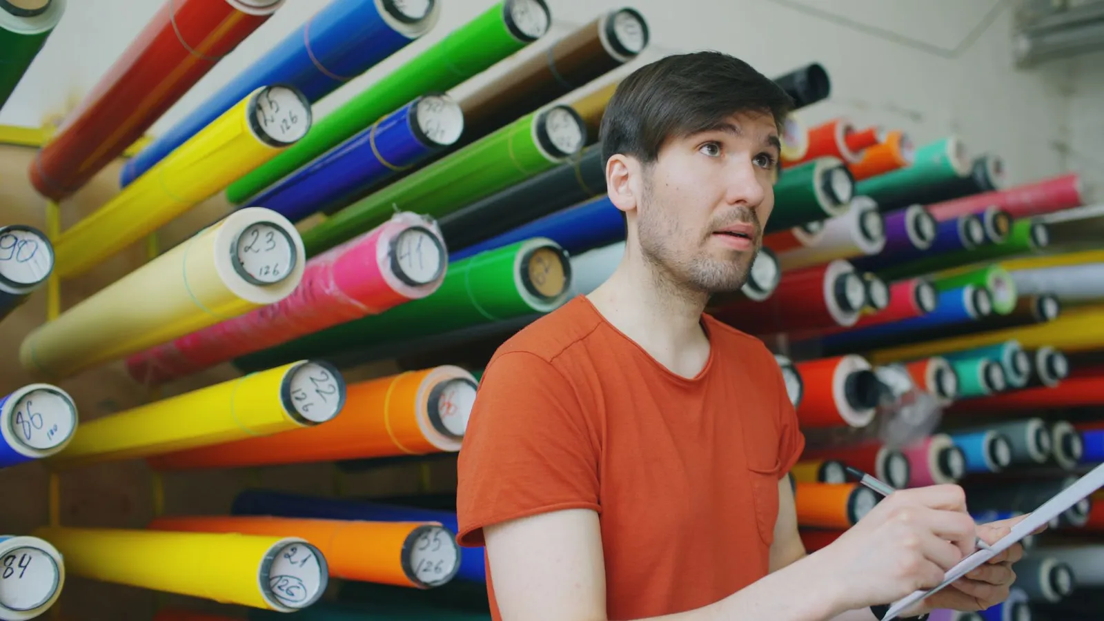 Man in workshop checking colorful vinyl rolls, representing creative work environment.