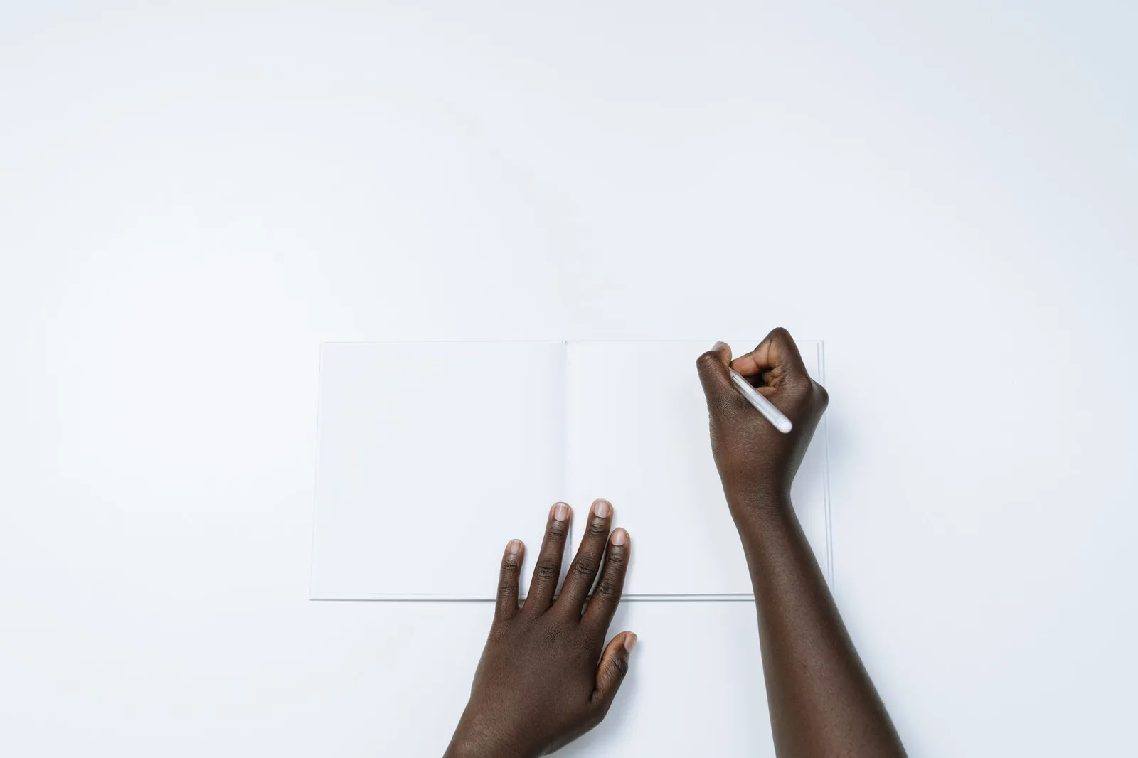 Top view of a person writing on a blank page in a notebook, showcasing simplicity and creativity.