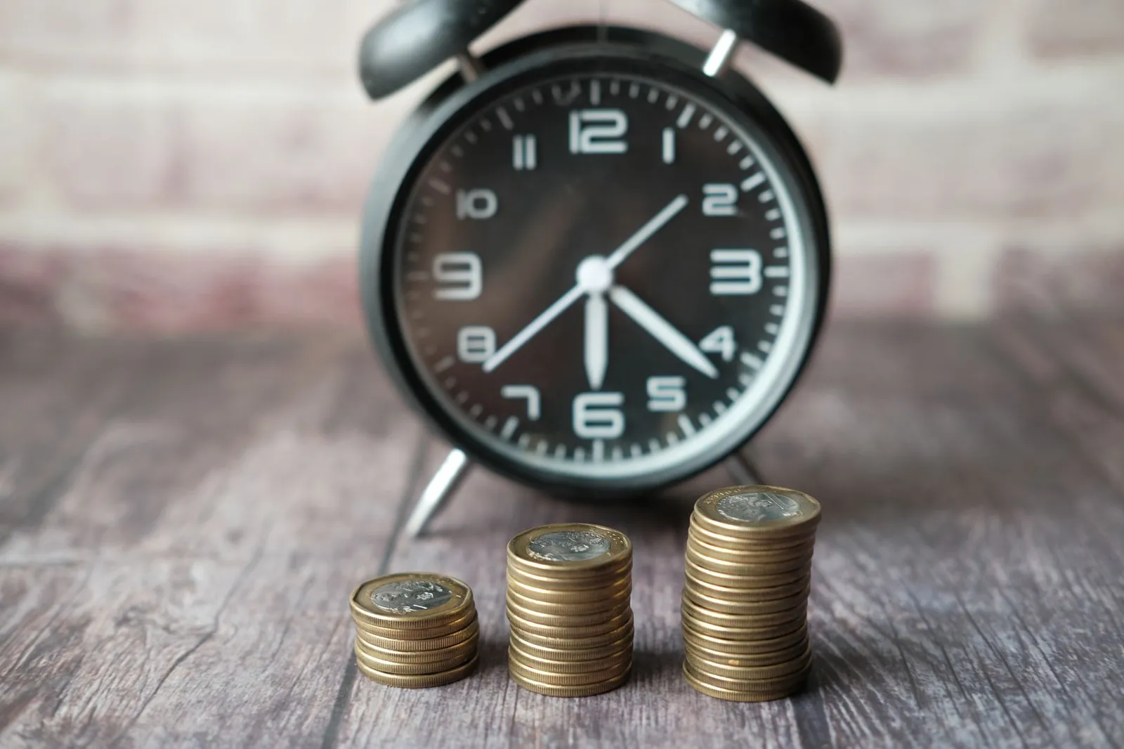 A close-up image of stacked coins with a blurred clock, symbolizing time and money relationship.