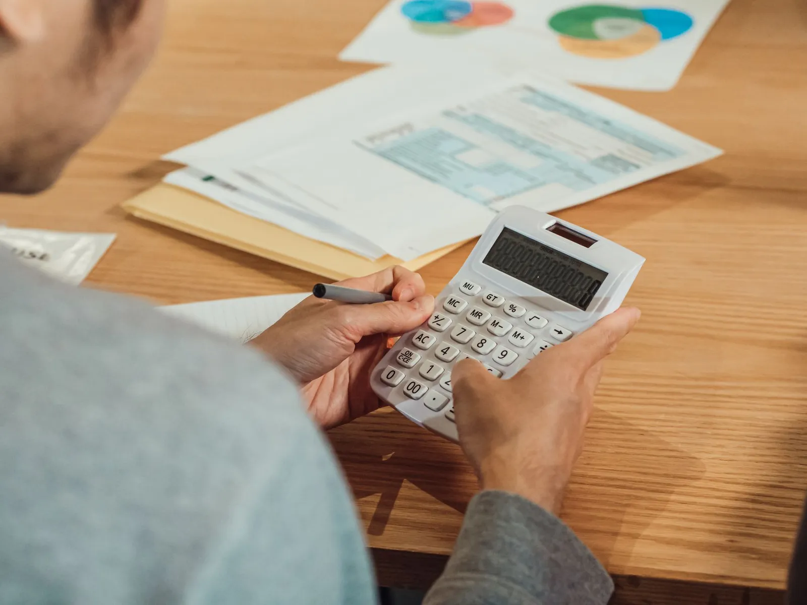 Focused image of a person using a calculator amidst financial documents and charts.