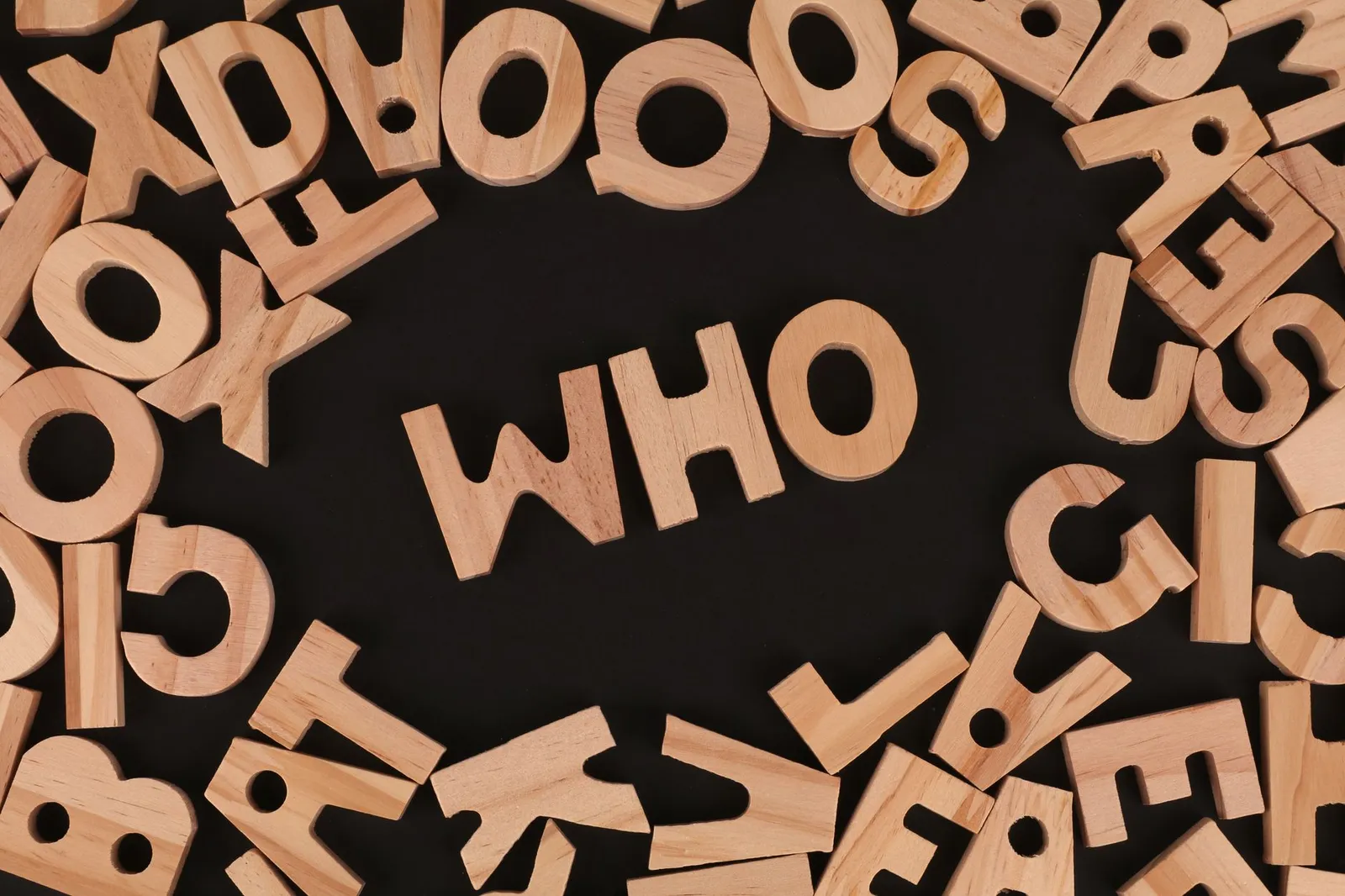 Wooden alphabet letters arranged to spell 'Who' on a black surface, creative message concept.