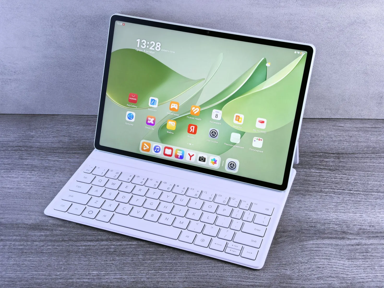 A modern tablet displaying a search engine logo next to a wireless keyboard on a wooden desk.