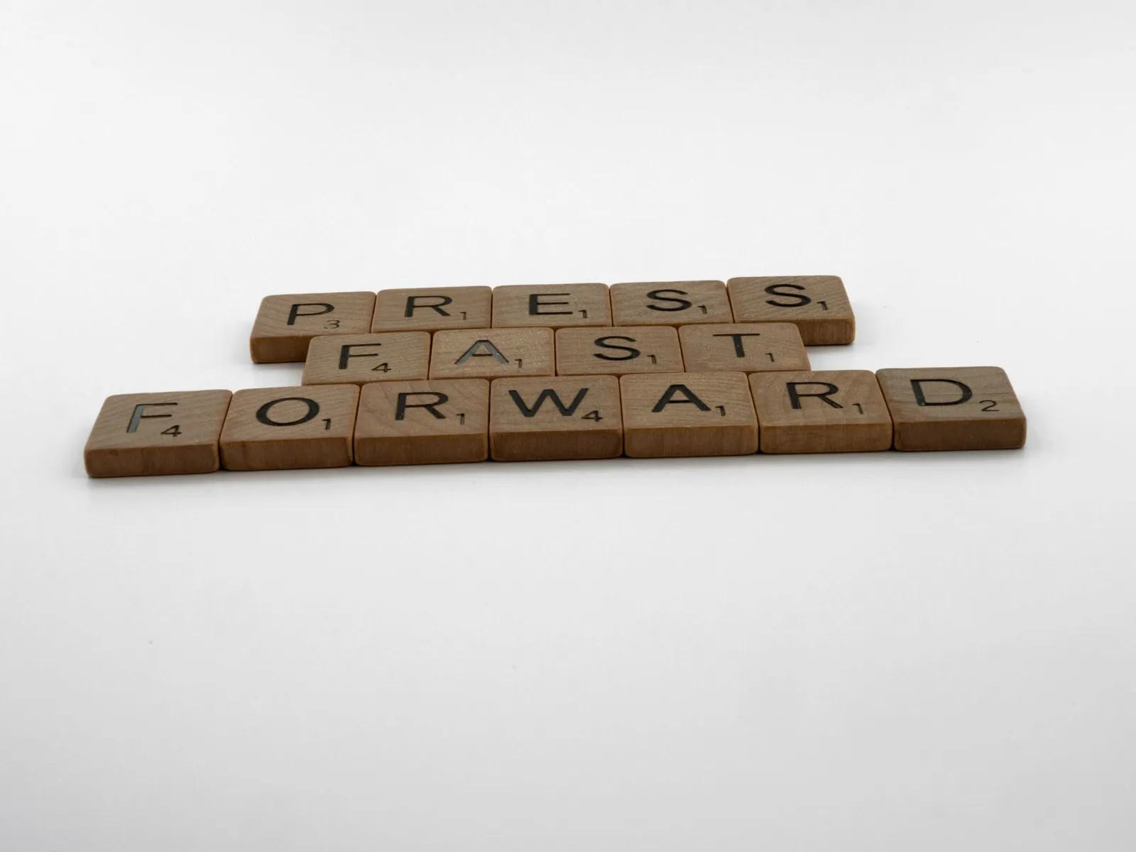 A motivational phrase 'Press Fast Forward' spelled with Scrabble pieces on a white background.