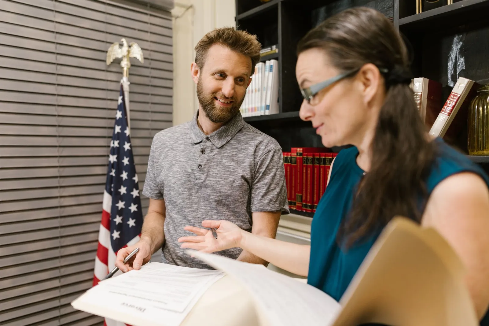 Two colleagues discussing documents in a formal office setting, featuring US flag decor.