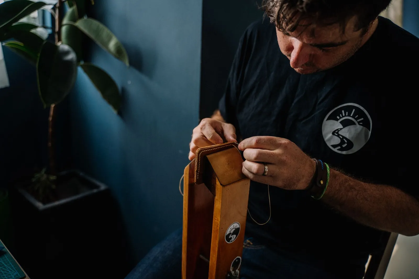 A skilled artisan concentrating on sewing a handmade leather bag, showcasing craftsmanship indoors.