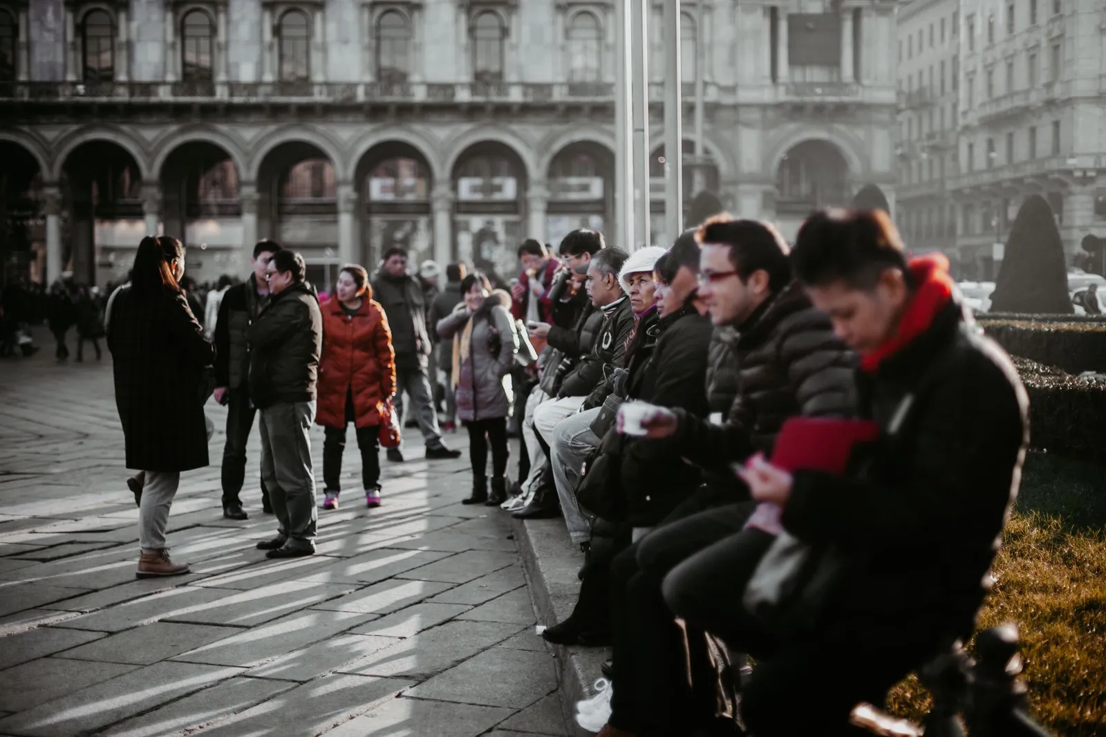A group of people in winter attire gathering in a street scene in Milan, Italy.