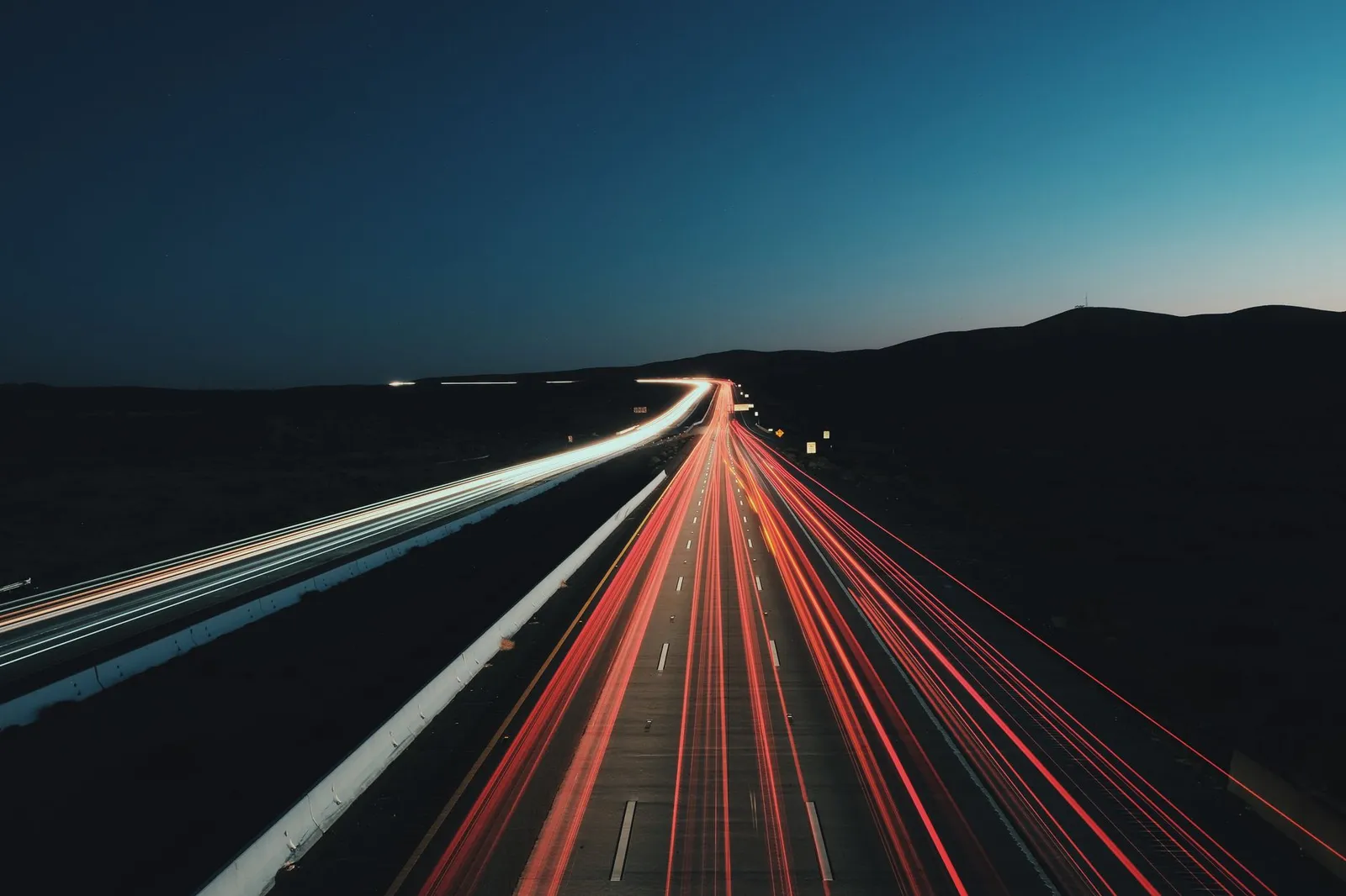Dynamic long exposure shot of highway light trails at night with a clear sky.